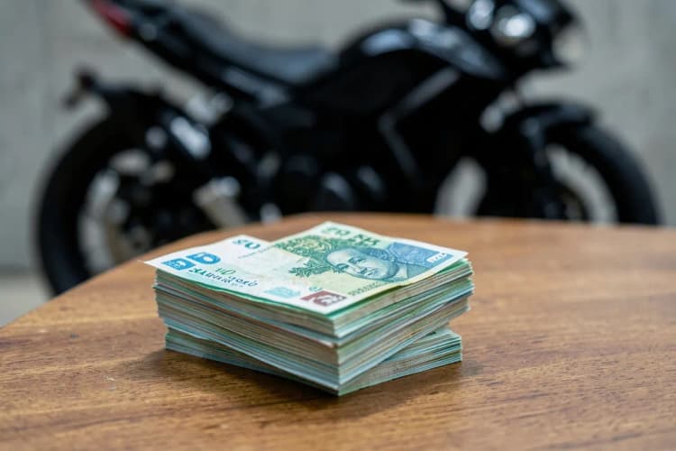 Um monte de notas de dinheiro empilhadas sobre uma mesa, com uma moto ao fundo desfocado.