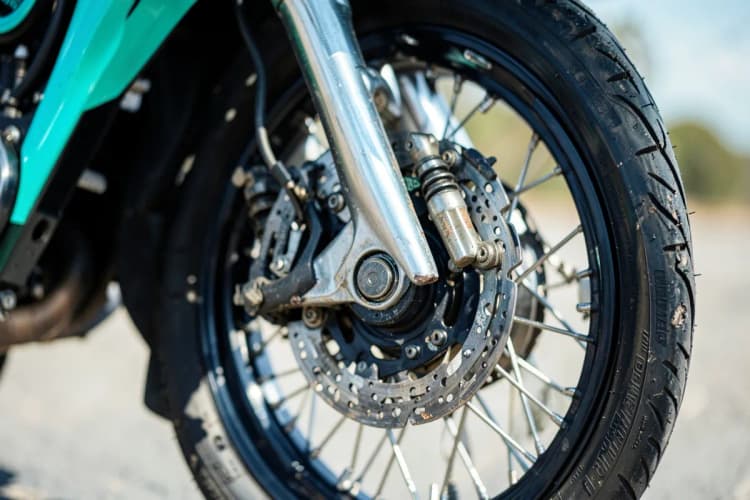 Uma moto sendo inspecionada antes de um passeio, com foco nas rodas e suspensão.