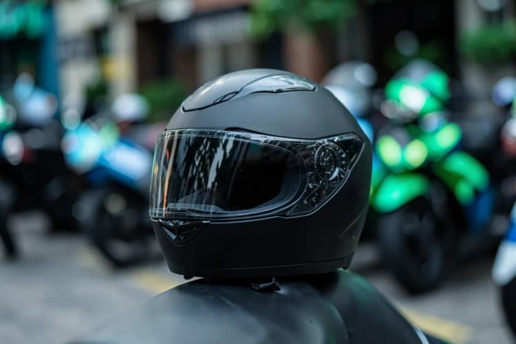 Uma mão segurando um capacete de moto preto sobre um fundo desfocado de motos alugadas.