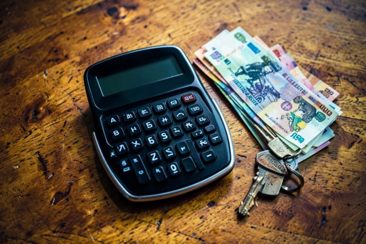 Uma calculadora e notas de dinheiro empilhadas sobre uma mesa de madeira com uma chave de moto ao lado.
