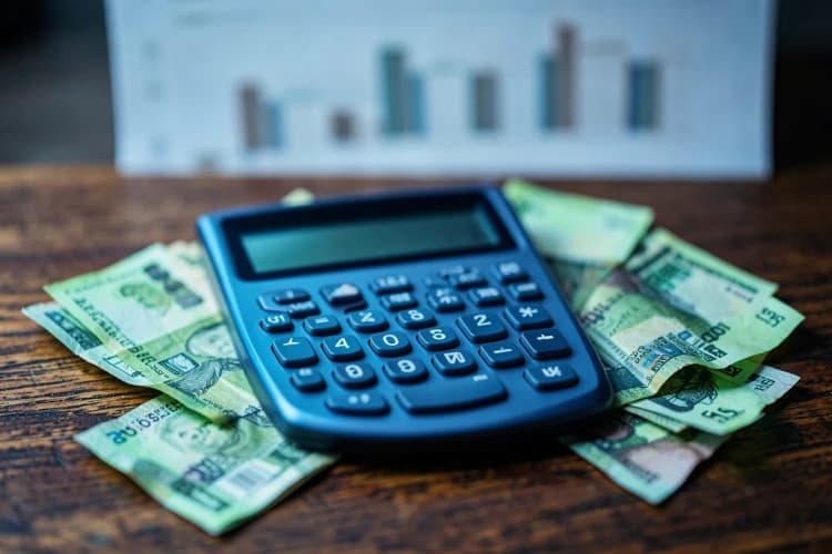 Calculadora e notas de dinheiro sobre uma mesa com um gráfico de barras desfocado ao fundo.
