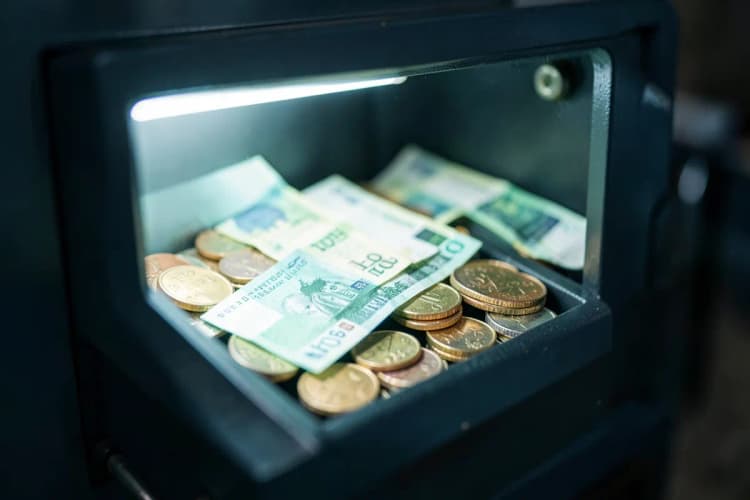 Uma pessoa organizando notas de dinheiro e moedas em um cofre.