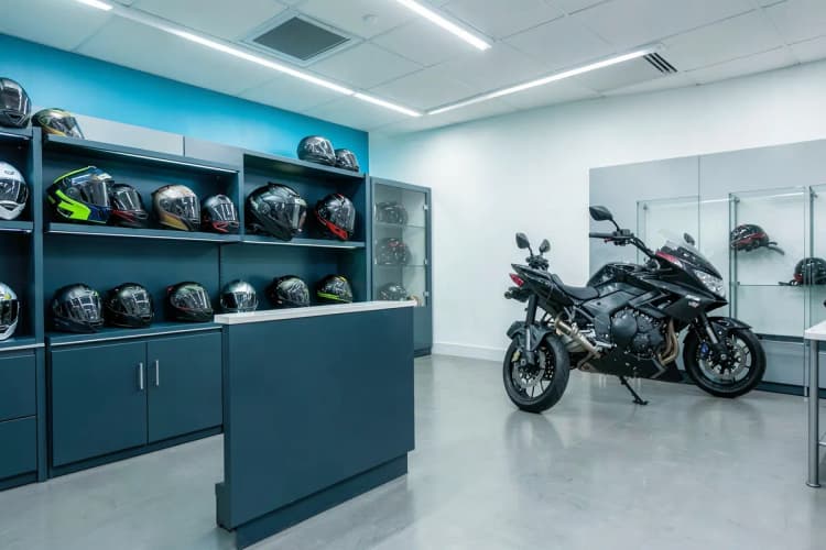 Um balcão de loja de aluguel de motos com capacetes organizados em prateleiras e uma motocicleta ao fundo.
